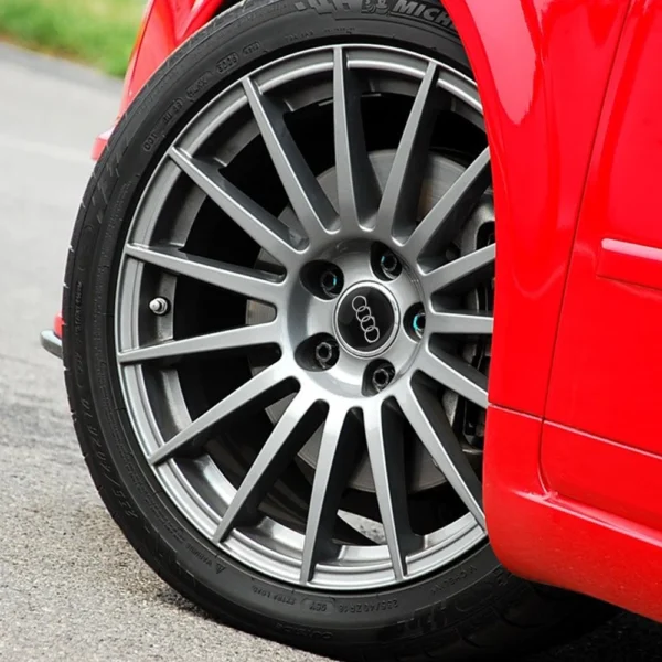 S13095741fbc448609e14405cfbd338e2T.webp Centre de roue Audi noir et argent installé sur une jante grise